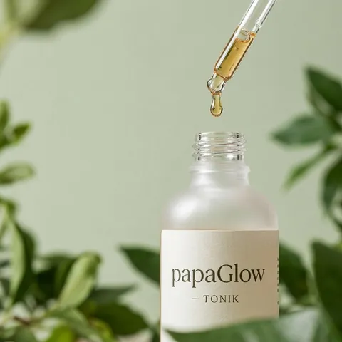 Złota kropla spada z pipety do otwartej butelki toniku papaGlow